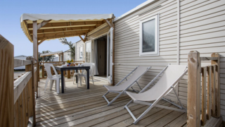 Terrasse en bois du Premium Mobile Home avec chaises longues, table à manger et auvent en bois.