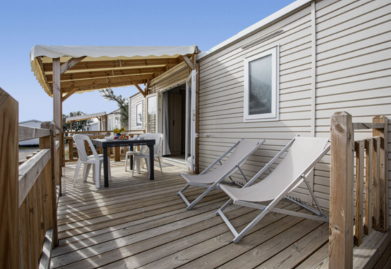 Træterrasse ved Premium Mobile Home med loungestole, spisebord, tagdækning og moderne facade.