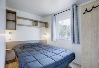 Premium Mobile Home soveværelse med dobbeltseng, reoler, vindue og lysgardiner på Seasonova Camping Barberousse.