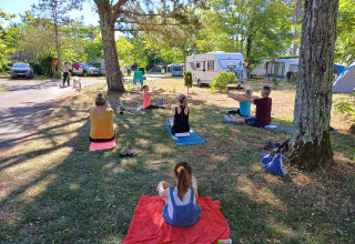 Menschen machen Yoga auf einer Wiese bei Wohnwagen im Seasonova Camping Le Lac de Cazaux in Occitanie, Frankreich.