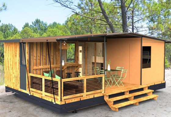 Kleine, moderne woning in het bos met houten veranda, buitenzitplaats en omringd door hoge bomen.