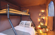 Cozy tiny house with a bunk bed, warm brown fabric walls, fairy string lights, and a small side window.