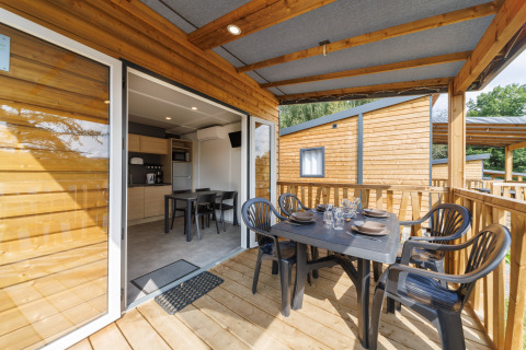 Überdachte Terrasse einer modernen Holzhütte mit gedecktem Tisch und Blick auf die offene Küche.