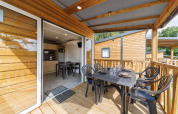 Terraza cubierta de una cabaña de madera con mesa de comedor y vista a una cocina moderna en el interior.