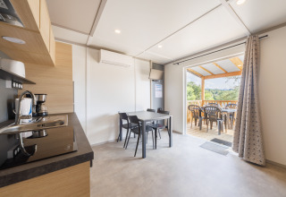 Moderne Lodge mit Küche, Esstisch und überdachter Terrasse mit Blick auf grüne Landschaft und Bäume.