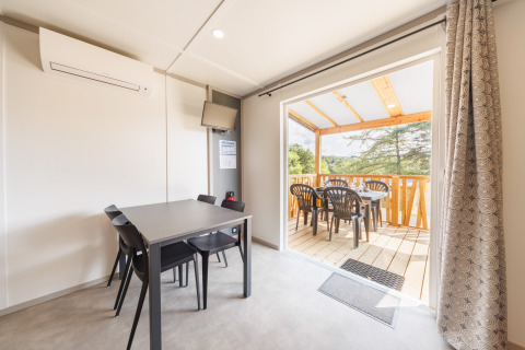 Modern lodge interior with dining area and open terrace, plastic chairs, and a scenic outdoor view.
