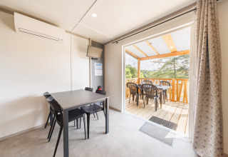 Modernes Lodge-Zimmer mit Essbereich, offener Terrasse, Kunststoffstühlen und Blick auf die Natur.