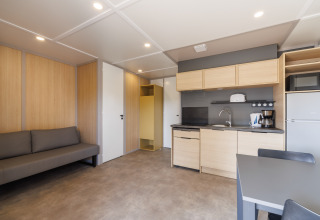 Modernes Lodge-Zimmer mit Küchenzeile, Kühlschrank, Sofa, Esstisch und hellem Innendesign.