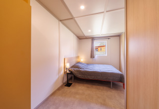 Modernes Schlafzimmer in einer Lodge mit Doppelbett, Nachttischen und Fenster mit Blick ins Freie.