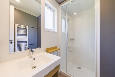 Modernes Badezimmer in einer Lodge mit Glasdusche, weißem Waschbecken und großem Spiegel am Fenster.