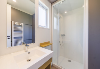 Modernes Badezimmer in einer Lodge mit Glasdusche, weißem Waschbecken und großem Spiegel am Fenster.