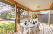 Überdachte Terrasse einer Lodge mit weißem Tisch, sechs Stühlen und ruhiger Aussicht ins Grüne.