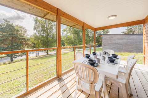 Überdachte Terrasse einer Lodge mit gedecktem Tisch, weißen Stühlen und Blick auf grüne Bäume.