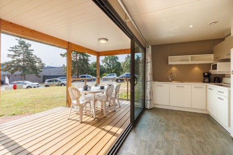 Cuisine lumineuse de lodge avec baie vitrée menant à une terrasse en bois et coin repas extérieur.