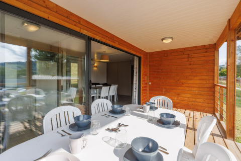 Essbereich einer Lodge im Freien mit Holzwänden, weißem Tisch, Geschirr und Blick ins Grüne.