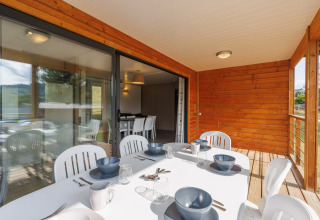 Udendørs spiseområde på en lodge med trævægge, hvidt bord, moderne service og naturskøn udsigt.
