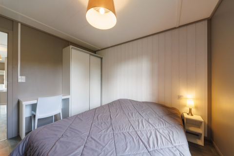 Schlafzimmer in einer Lodge mit Doppelbett, Nachttischlampe, Kleiderschrank und Schreibtisch.