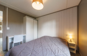 Lodge bedroom featuring a double bed, a bedside table with a lamp, a wardrobe, and a desk with chair.