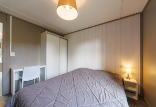 Schlafzimmer in einer Lodge mit Doppelbett, Nachttischlampe, Kleiderschrank und Schreibtisch.