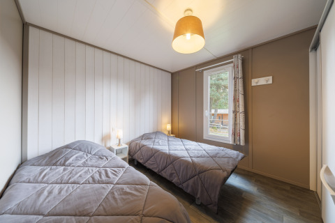 Gemütliches Schlafzimmer in einer Lodge mit zwei Einzelbetten, grauen Decken und viel Tageslicht.