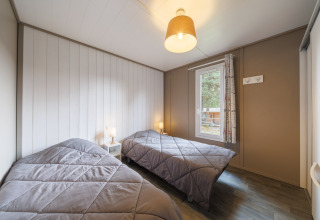 Gemütliches Schlafzimmer in einer Lodge mit zwei Einzelbetten, grauen Decken und viel Tageslicht.