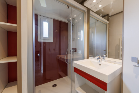 Salle de bain moderne dans un lodge, cabine de douche vitrée, lavabo blanc, étagères et miroir mural.