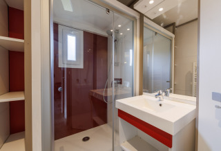 Modernes Badezimmer in einer Lodge mit Duschkabine, Waschbecken, Spiegel und roten Akzentwänden.