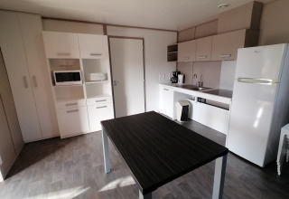 Moderne Küche im Cottage Premium des Camping Holiday Park Les Demeures du Lac mit Tisch und Geräten.