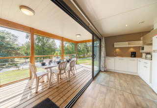 Cocina luminosa y terraza cubierta con comedor en una cabaña, con vistas a árboles y naturaleza exterior.
