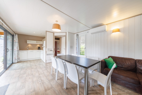 Bright lodge interior with an open kitchen, dining area, brown sofa, and sliding glass doors to the deck.