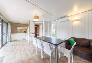 Helles Lodge-Wohnzimmer mit moderner Küche, Esstisch, braunem Sofa und großen Fenstern zur Terrasse.