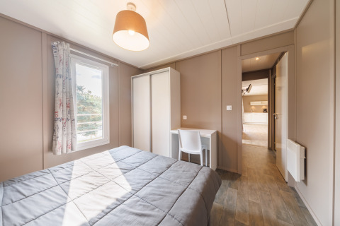 Helles Schlafzimmer in einer Lodge mit Doppelbett, Schrank, Schreibtisch, Fenster und beigen Wänden.