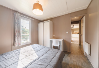 Helles Schlafzimmer in einer Lodge mit Doppelbett, Schrank, Schreibtisch, Fenster und beigen Wänden.