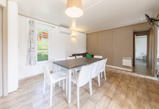 Lichte en moderne eetruimte in een lodge met zes witte stoelen, houten vloer en ruime vensters.