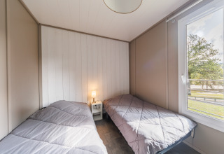 Habitación luminosa en una cabaña con dos camas individuales, mesa de noche con lámpara y gran ventana.