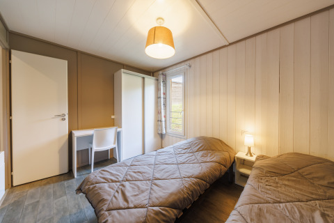 Et hyggeligt værelse i en lodge med to enkeltsenge, skrivebord, stol, garderobe og vindue med lys.