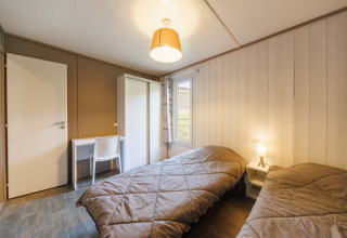 Acogedora habitación en una cabaña con dos camas individuales, escritorio, silla, armario y ventana.
