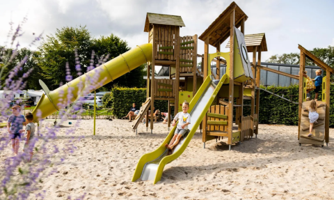 Children play on a large playground with slides and sand at Campsite de Witte Berg holiday park in Overijssel, Netherlands.