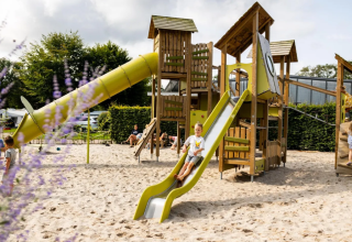 Children play on a large playground with slides and sand at Campsite de Witte Berg holiday park in Overijssel, Netherlands.