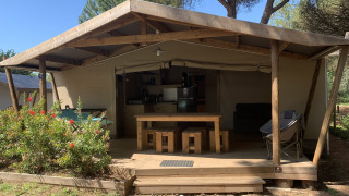 Tenda safari presso Log Cabin Cotton Comfort con veranda in legno, cucina e area relax all’aperto.