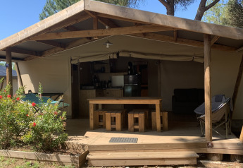 Safari tent at Log Cabin Cotton Comfort with wooden patio, kitchen, outdoor seating, and natural surroundings.