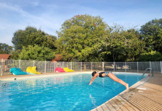 En person dykker i en swimmingpool ved Camping le Roc i Occitanie, Frankrig, omgivet af farverige sækkestole.
