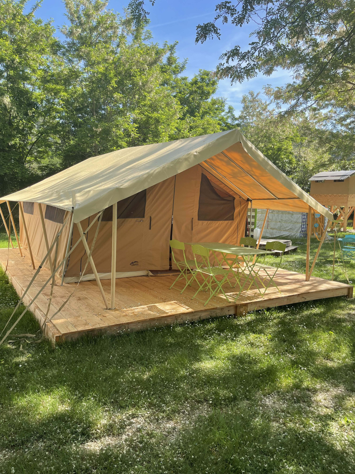 Indiana safari tent op houten platform met tafel en stoelen, omringd door bomen en groen gras