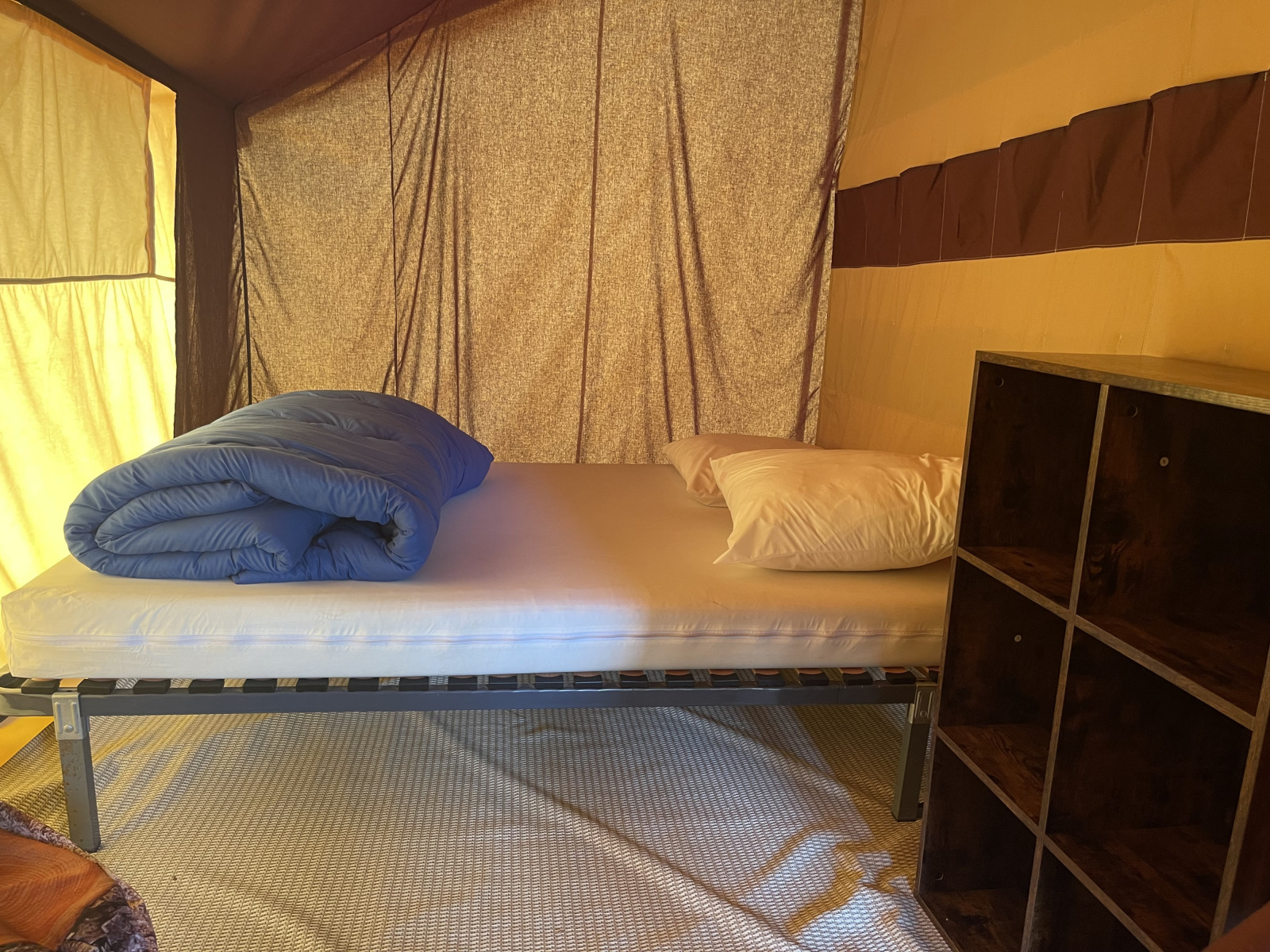 Binnenzicht van Indiana Tent op Camping Paradis Family des Issoux met bed, blauwe deken en kast.