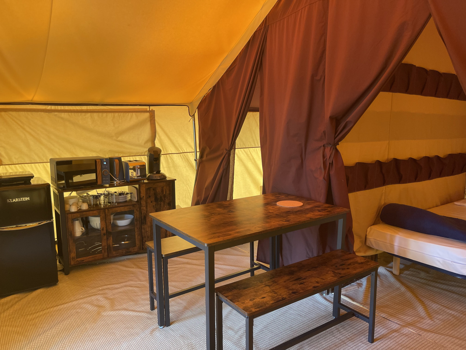 Interieur van Indiana Tent bij Camping Paradis Family des Issoux met eettafel, keuken en bed.