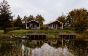 Dos encantadoras cabañas junto a un lago, con muelles pequeños y rodeadas de naturaleza y árboles.