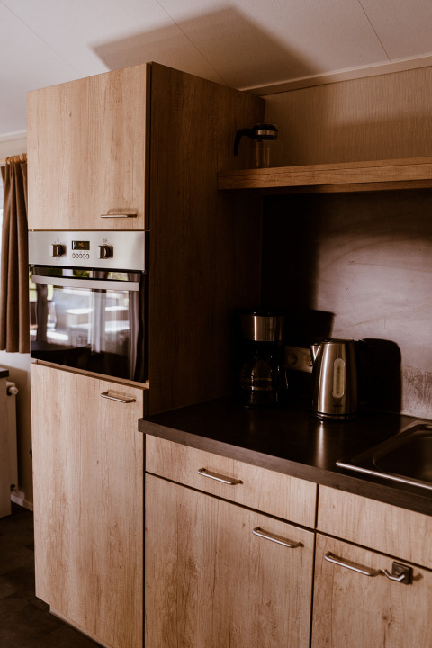 Modern kitchen area with wooden cabinets and appliances in Chalet lodge at Holiday park Eigen Wijze, Netherlands.