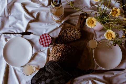 Frühstückstisch in einer Lodge mit Brot, Saft, Marmelade, zwei Tellern und gelben Blumen.
