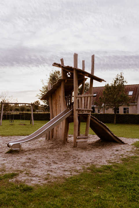 Natürlicher Spielplatz mit Holzkletterturm und Rutsche an einer Glamping-Unterkunft auf einer Wiese.