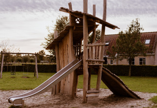 Aire de jeux rustique avec structure en bois et toboggan près d’un site de glamping entouré d’herbe.